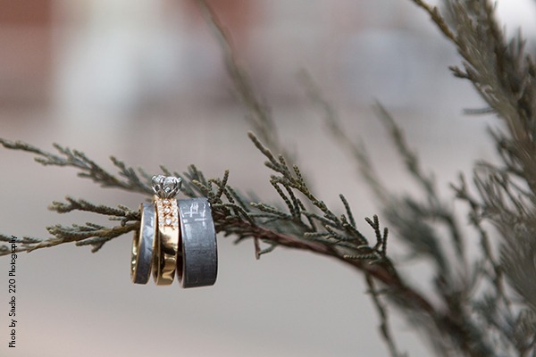 Gray wedding band and rose gold engagement ring on pine tree