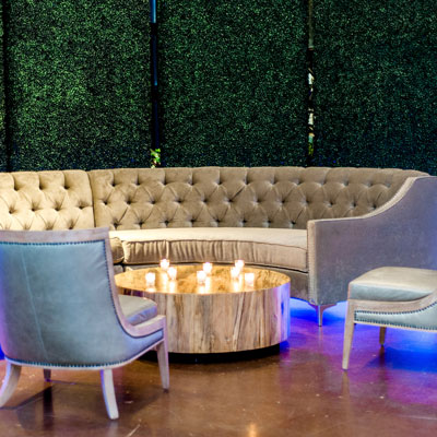 Wedding lounge with curved gray sofa and wooden circular table by Haven & Gather