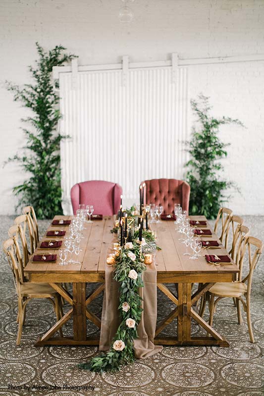 Modern, rustic table setting with maroon and greenery accents