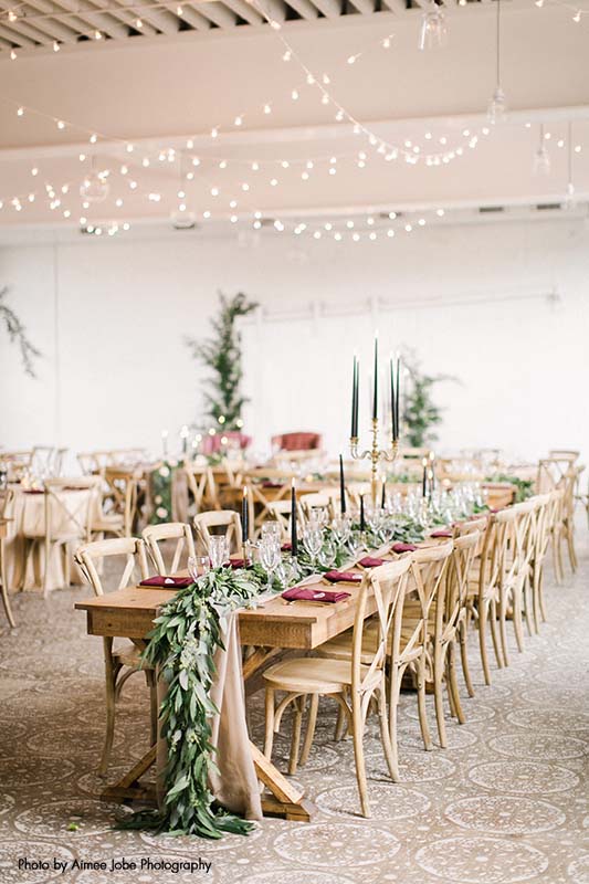 Modern rustic table seating with accents of maroon and greenery