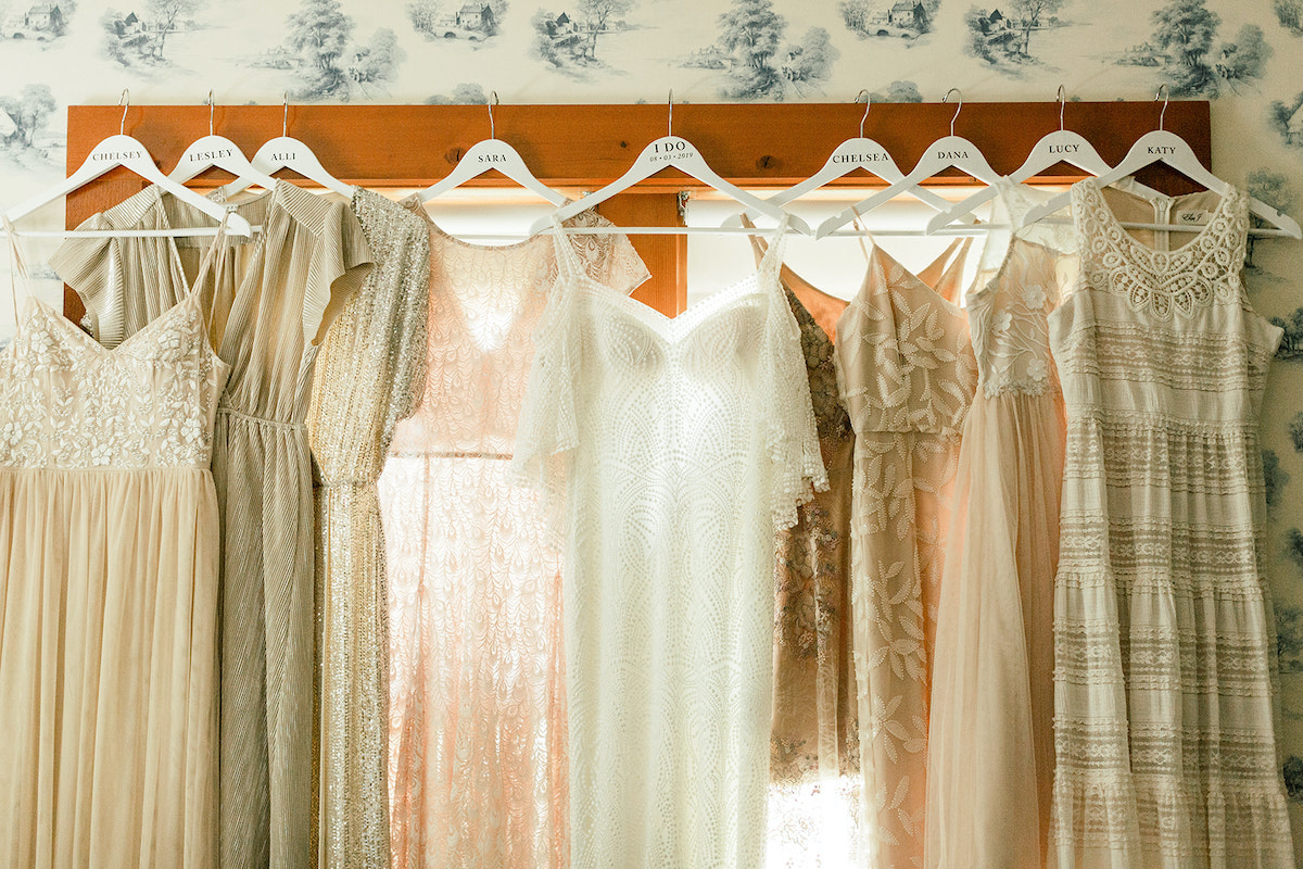 Wedding dress and neutral-toned gowns sit on hangers at boho barn wedding