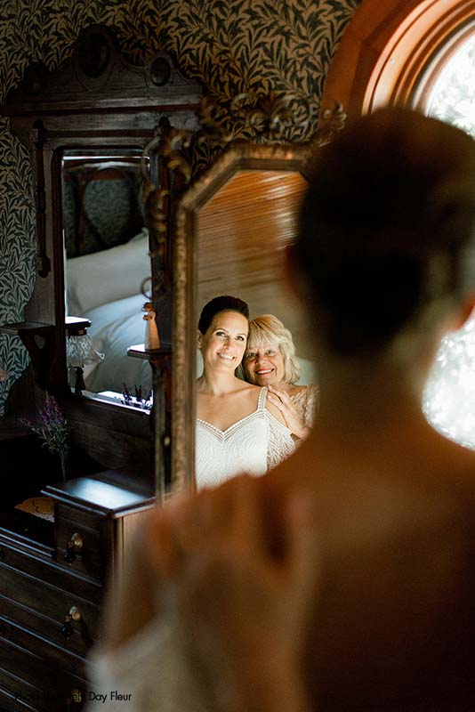 Bride and mother pose in a mirror before wedding