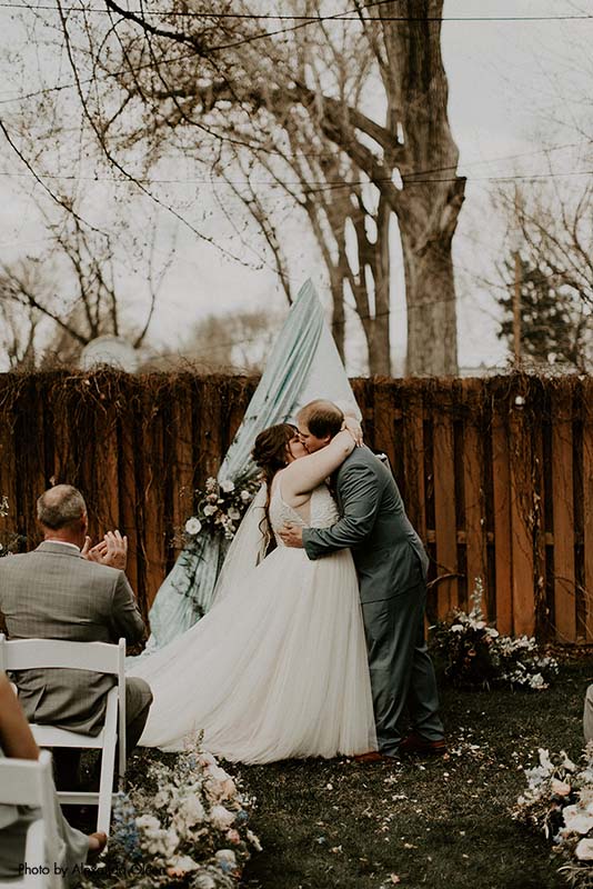 Bride and groom share first kiss at backyard micro wedding