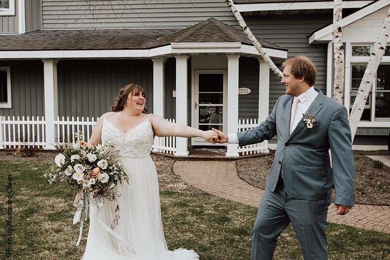 Bride in blush dress and groom in blue suit outside of house
