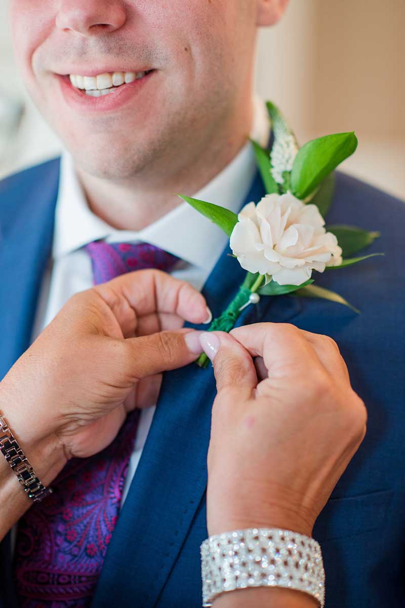 White rose boutonniere with greenery on blue suit