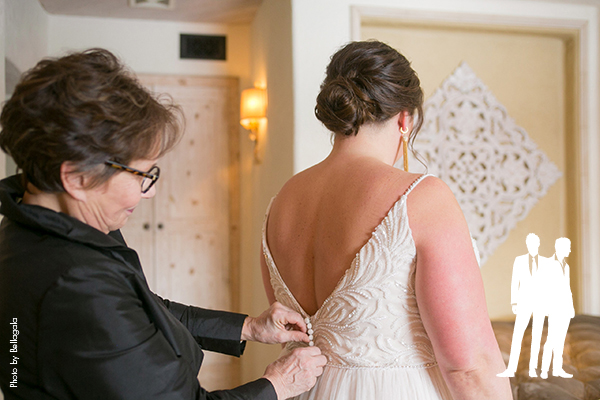 Mother helping bride button her wedding dress