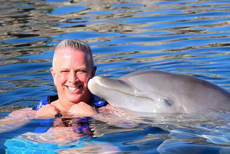 Dolphin kisses man on cheek with swimming