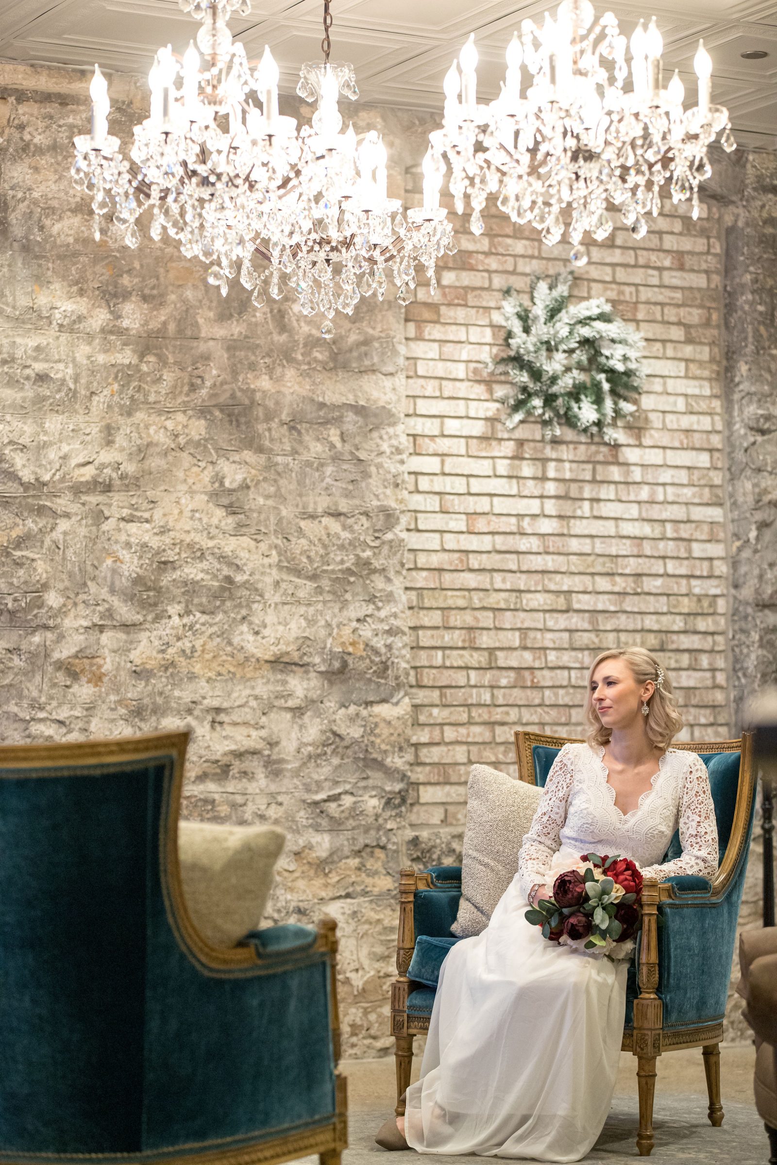 Bride sits in front of historic brick wall with two chandeliers about her at St. James Hotel