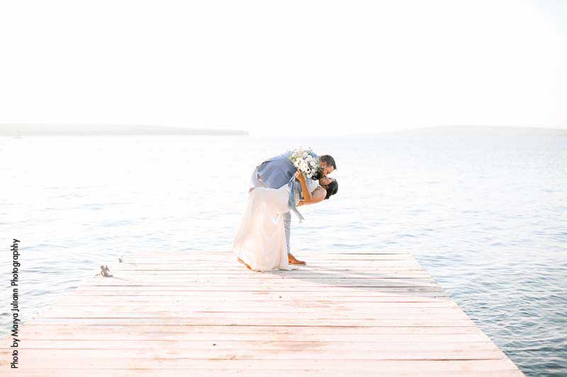 Bride and groom kiss on lakeside dock