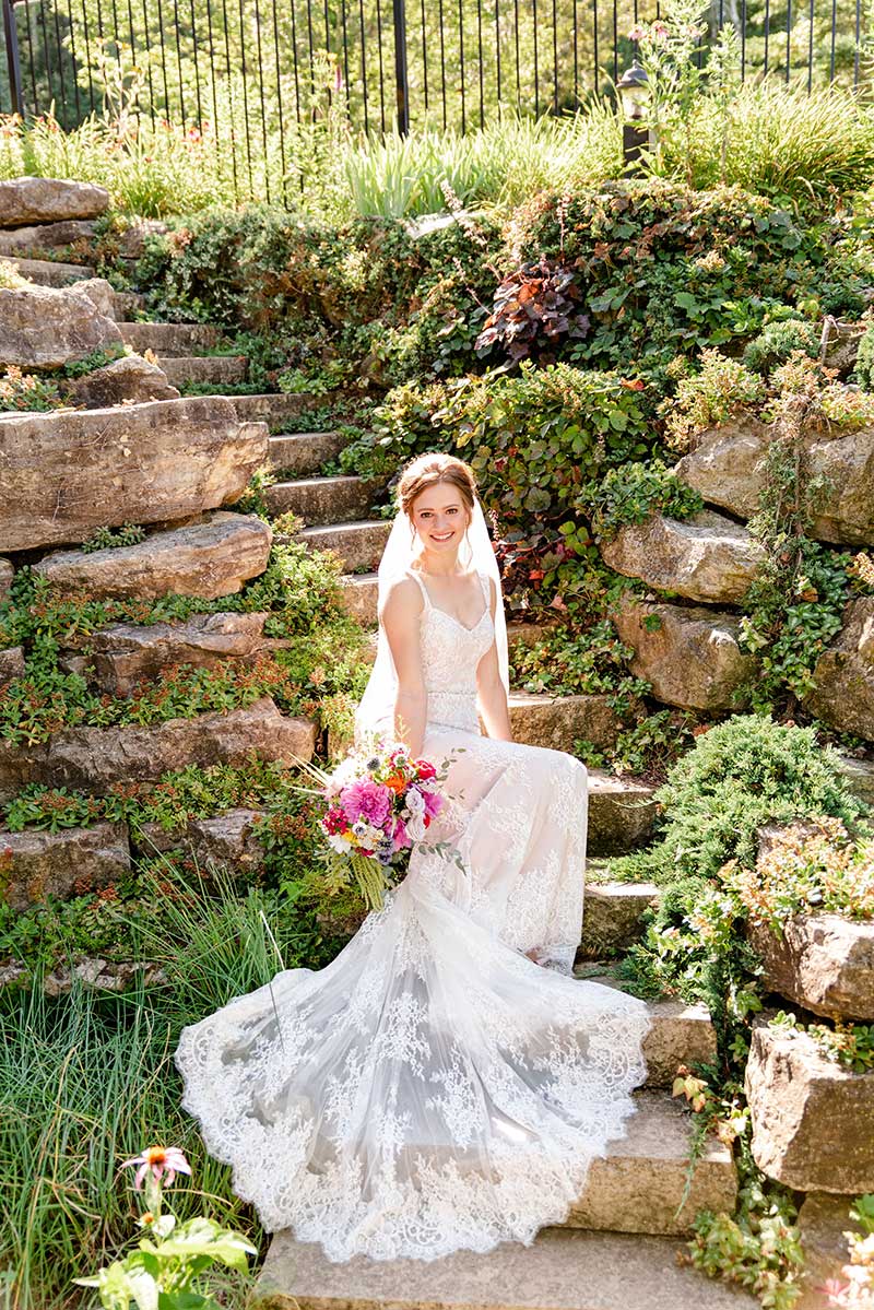 Bride sits on stone stairs with greenery 