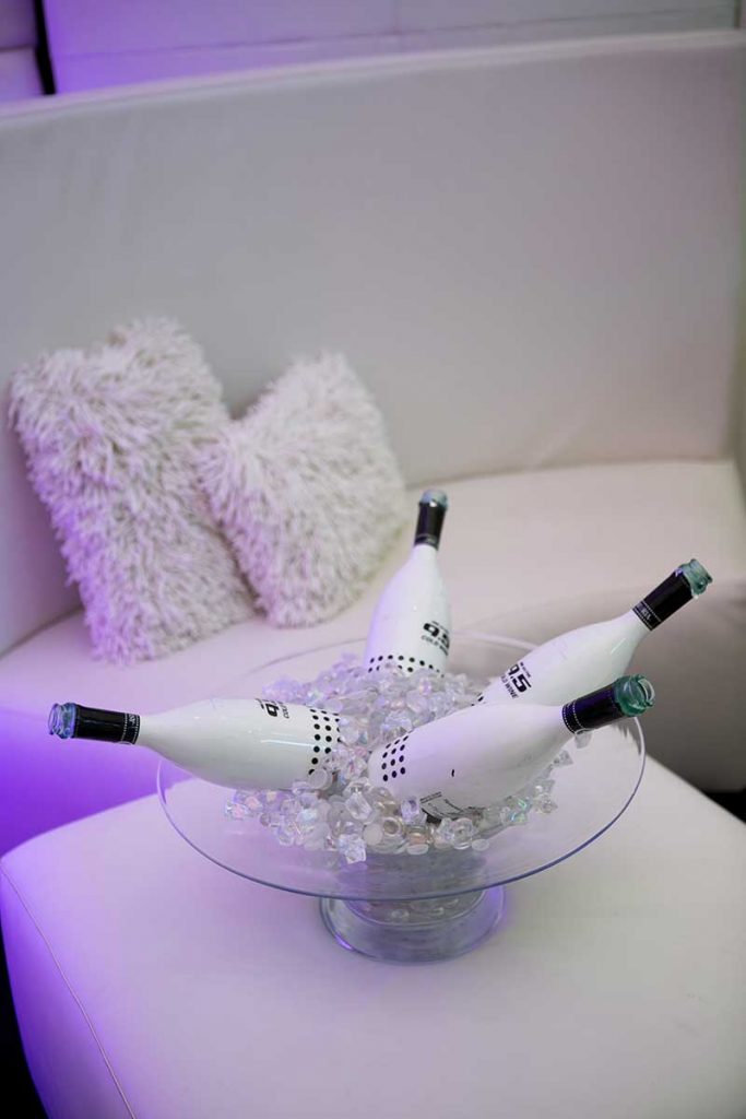 Lounge at wedding with white couch, pillows, and coffee table and black and white champagne bottles