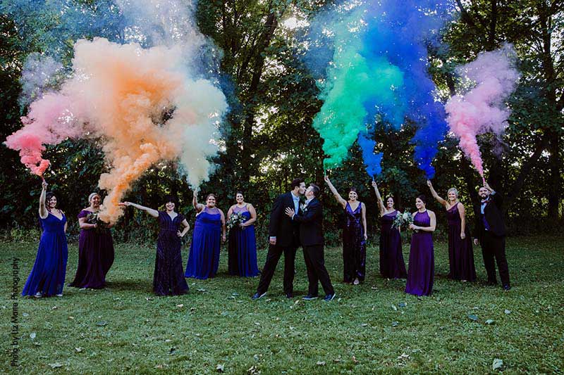Bridal party holds rainbow smoke bombs as grooms kiss