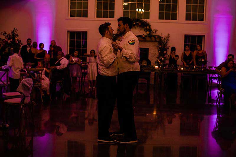 Grooms share first dance with purple uplighting in background