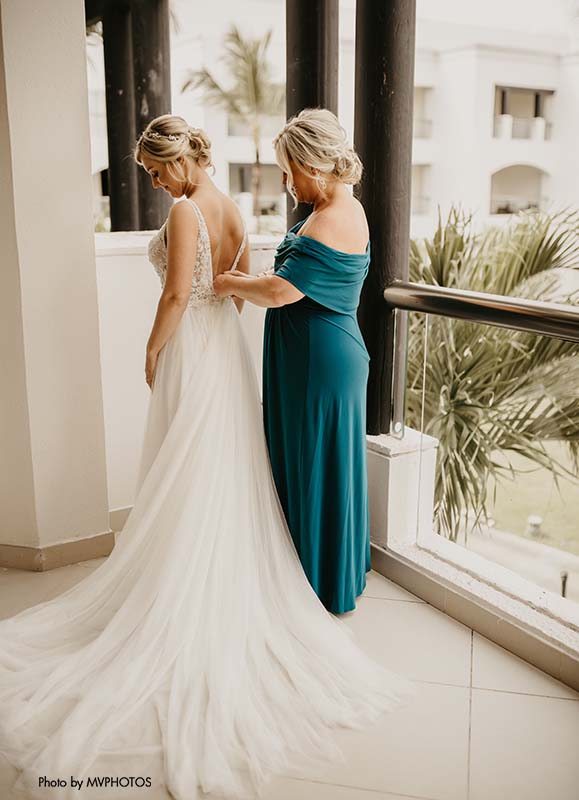 Mother of the bride in turquoise dress helps bride zip up her dress