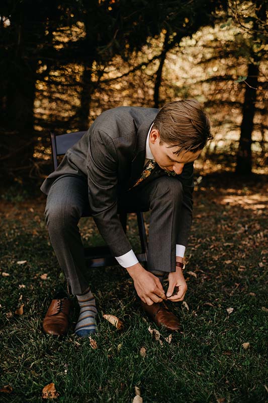 Groom ties shoes in charcoal suit