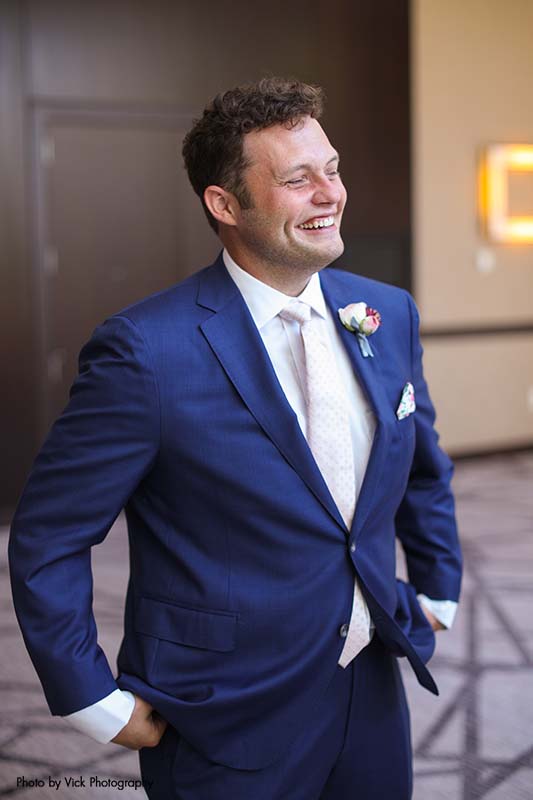 Groom wearing a blue suit with a pink tie for summer wedding