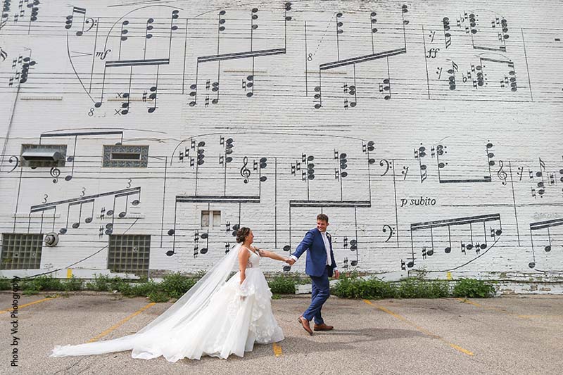 Bride and groom taking pictures in front of a music sheet wall
