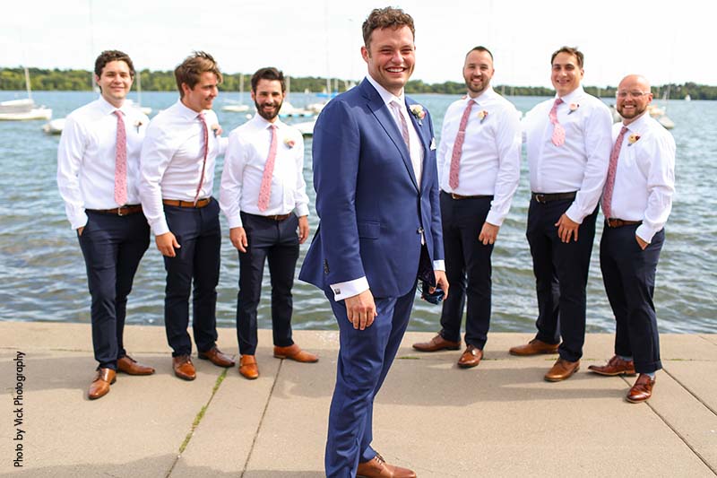 Groom wearing blue suit in front of lake