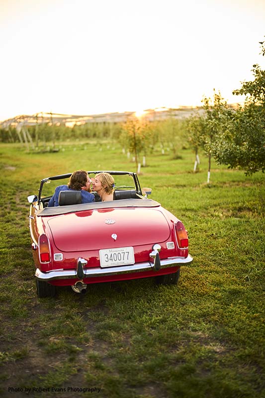 Bride and groom drive off in small red convertible