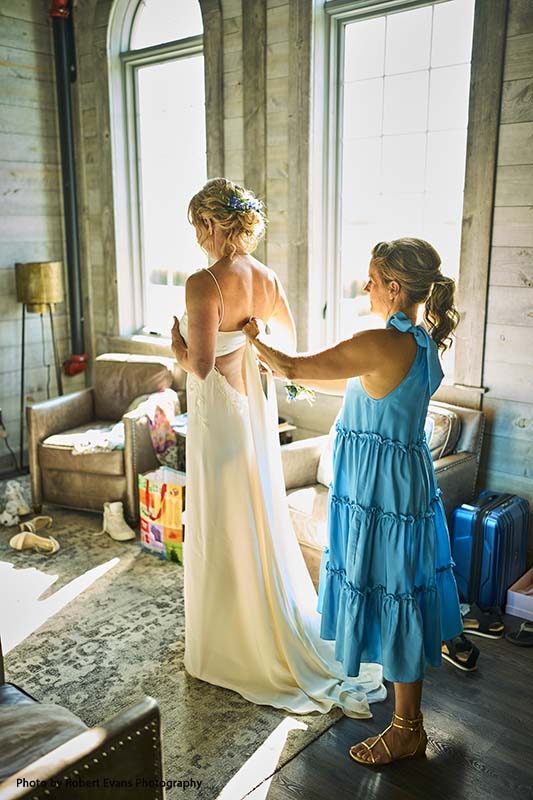 Maid of honor in blue dress helps bride zip gown