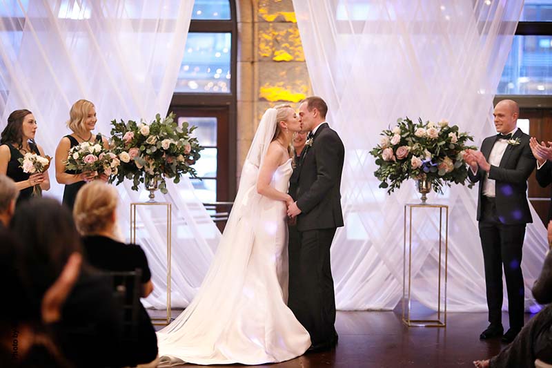 Bride and groom first kiss at ballroom wedding