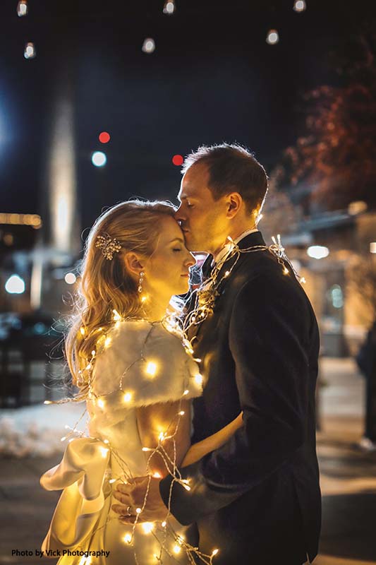 Bride and groom wrapped in string lights