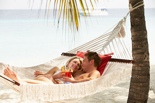 Couple sits in hammock on beach for honeymoon planned by Travel Leaders