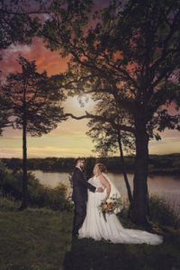 Bride and groom pose by a lake
