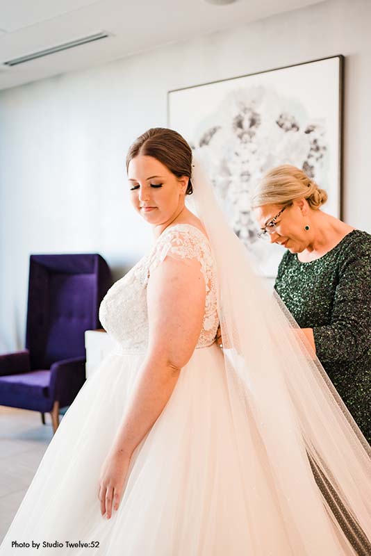 Mother helping bride button her wedding dress
