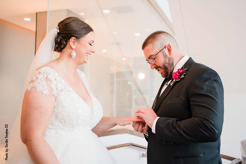 Groom putting ring on bride at ballroom wedding