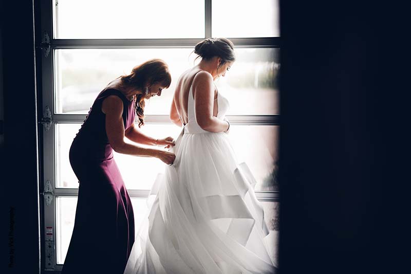Mother helping bride zip wedding dress