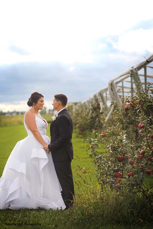 Bride and groom taking pictures in front of apple orchard