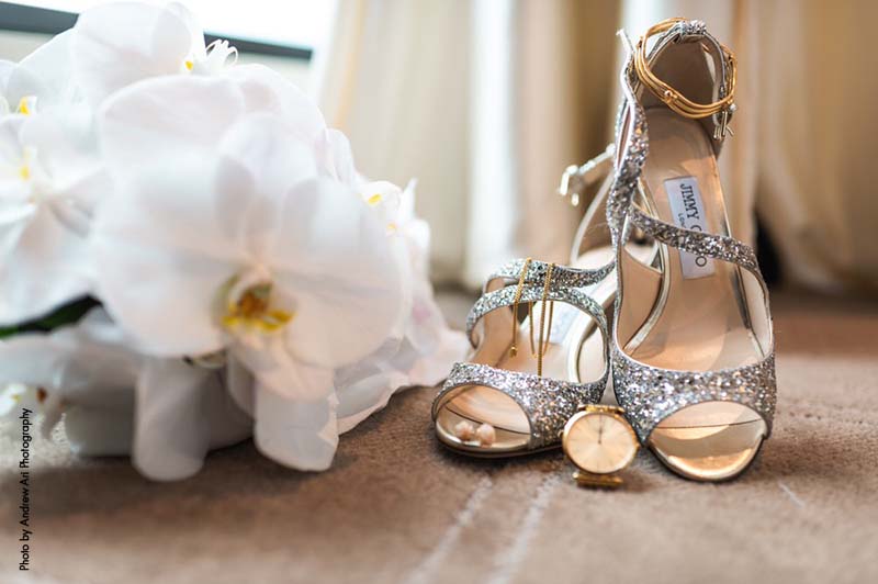 Silver open-toed shoes sit next to white orchid bouquet