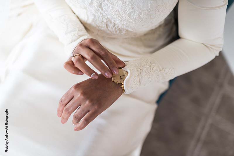 Bride in long-sleeve white wedding gown puts on a gold watch