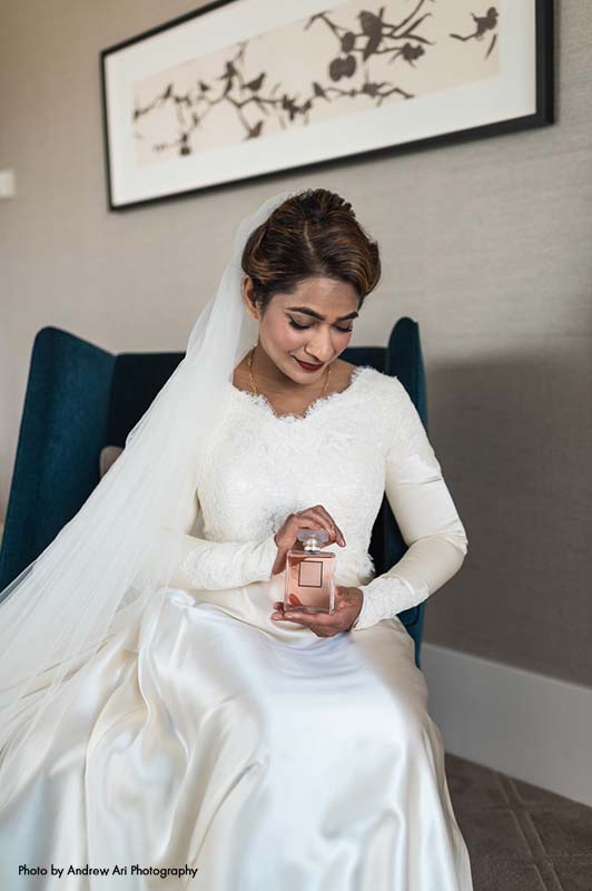 Bride in classic long-sleeve silk gown holding perfume