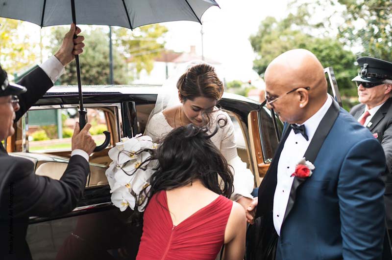 Father of the bride in Navy suit helps bride out of a car