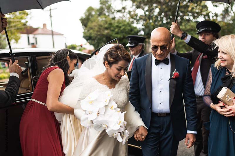 Father of the bride takes his daughter's hand as she walks out of vintage car
