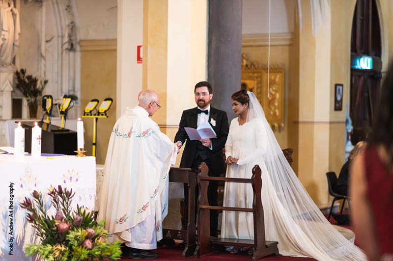 Bride and groom stand next to priest during ceremony