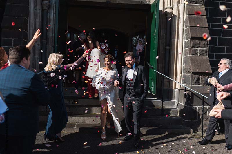 Guest throw rose petals at bride and groom as they exit a church