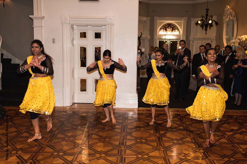 Bollywood dancers in yellow skirts and black tops dance at wedding reception