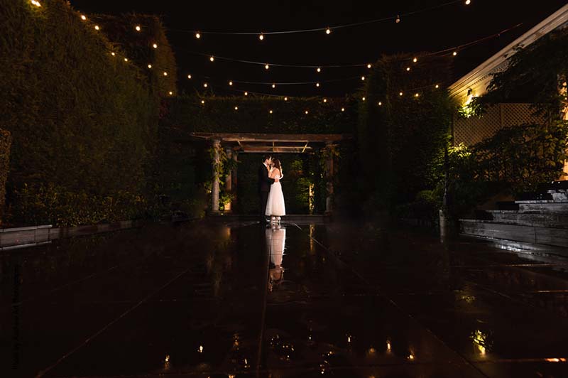 Bride and groom stand under twinkling lights in a dark room