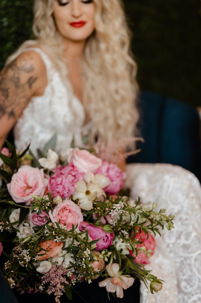 Bride with long blonde hair sits with large pink and greenery bridal bouquet