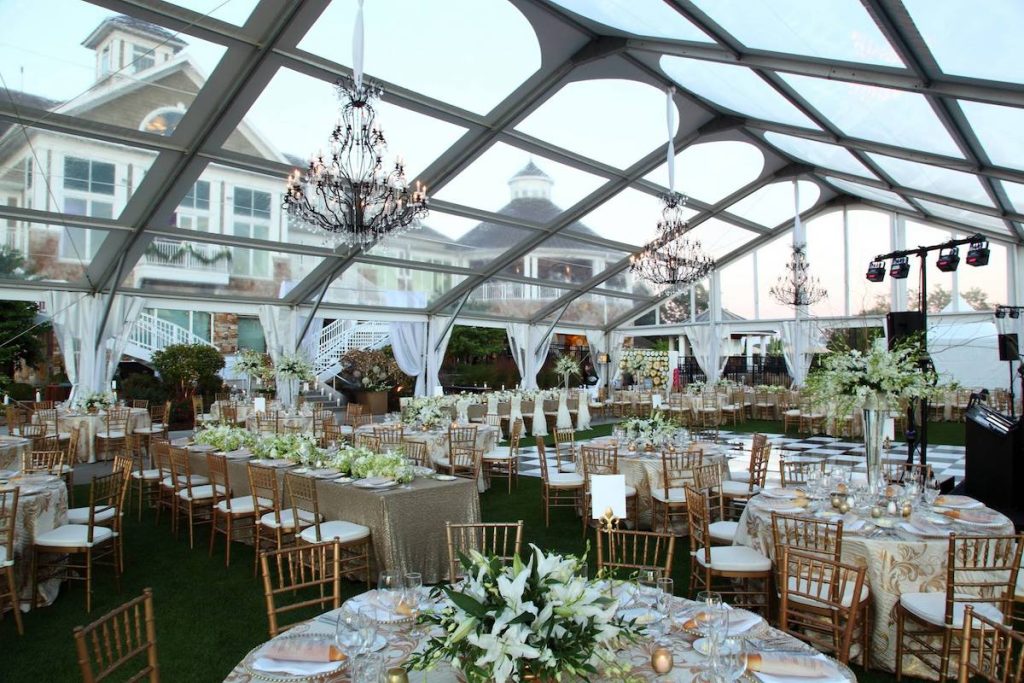 See-through outdoor wedding tent with gold chairs and greenery centerpieces