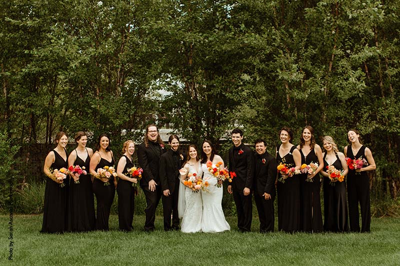 Mixed gender wedding party in all black stand with brides