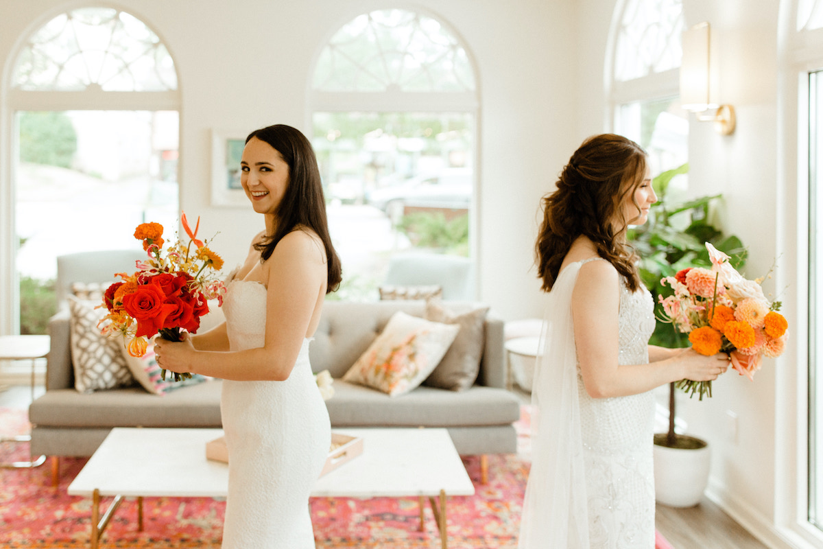 Brides stand back to back holding vivid flowers