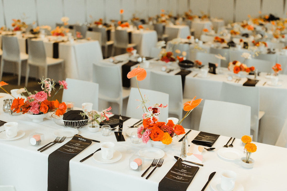 Art-inspired wedding reception with bright floral centerpieces and black flatware and menus