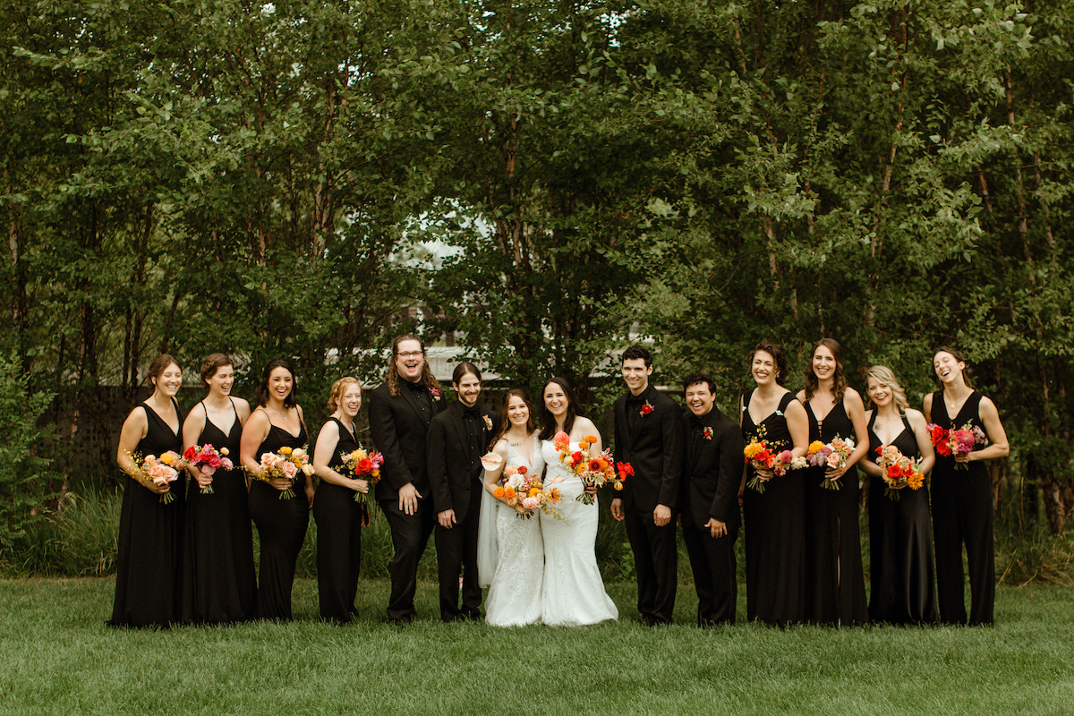 Two brides stand with wedding party wearing all black for an art-inspired wedding