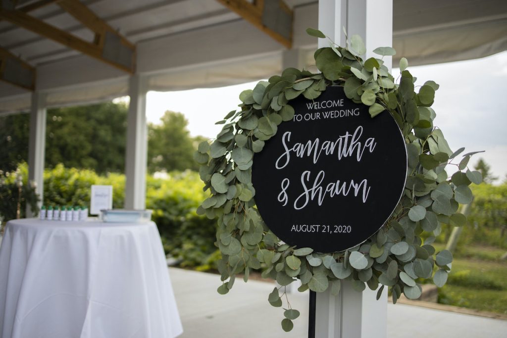 Black and white circular wedding welcome sign with eucalyptus wrapped around it 