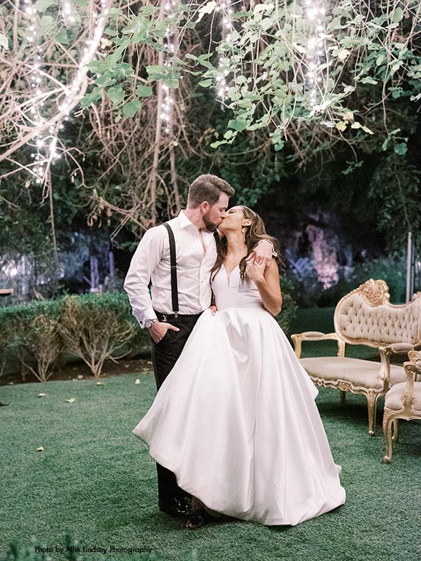 Bride and groom kiss under a tree with twinkling lights