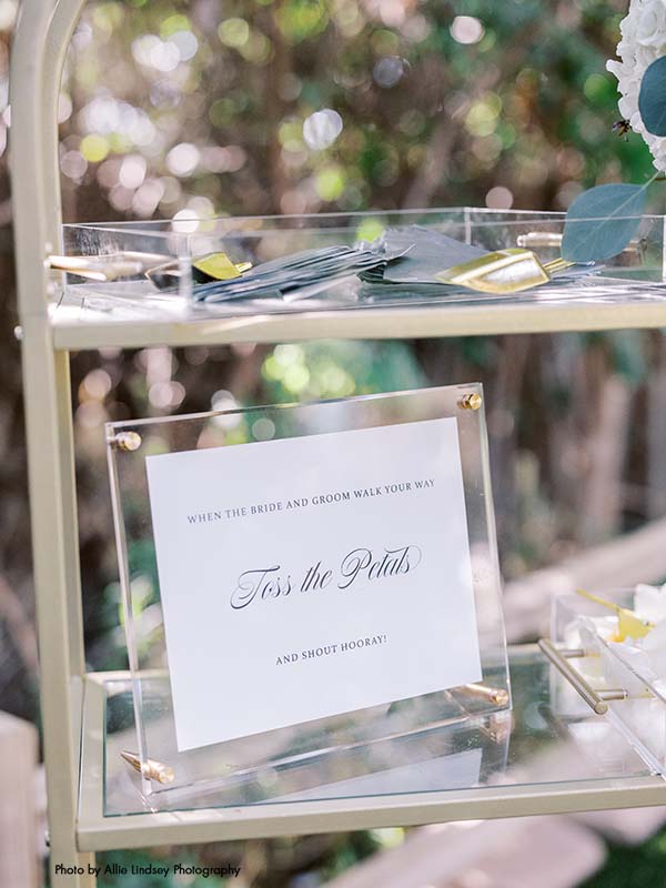Sign sitting on a glass shelf that says "toss the petals" after wedding ceremony